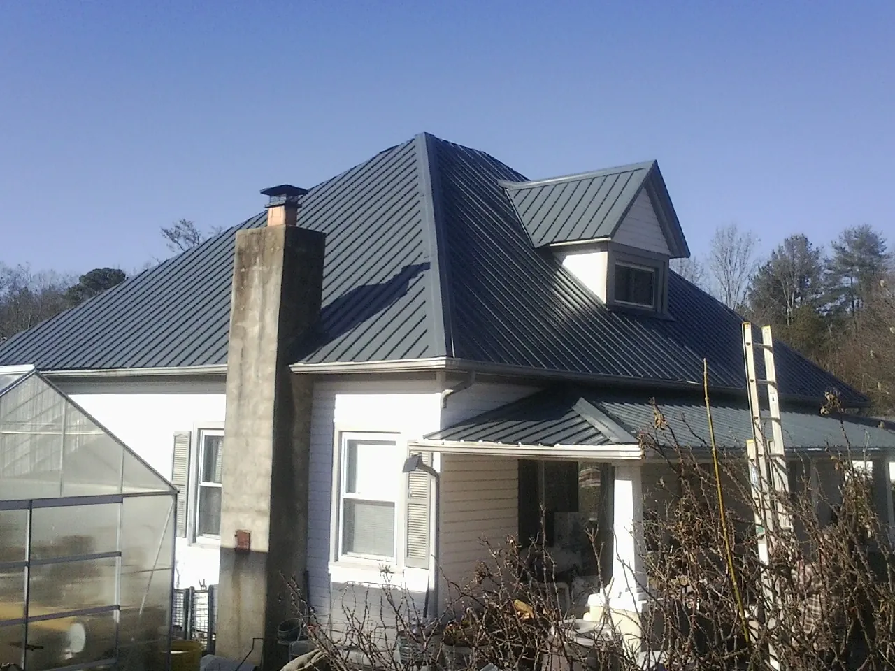 Dark blue standing seam metal roof on a white farmhouse with dormer — Slate & Tile Roof Repair by Roofing Brothers in Burlingham