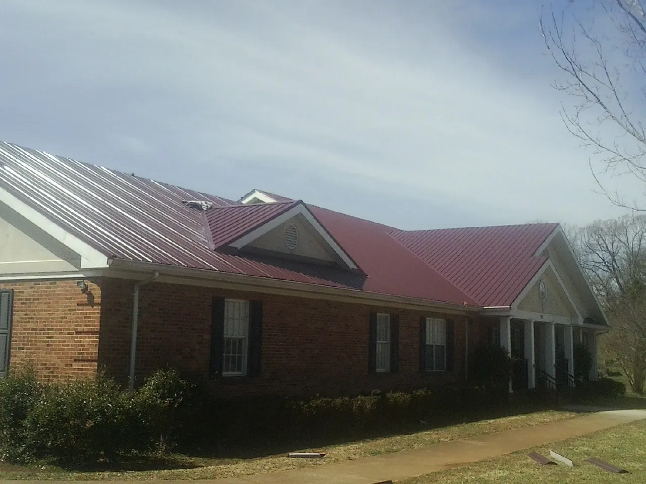 Red metal roof with gabled entries on a long brick building, from a Hail Damage Roof Repair job in Burlingham