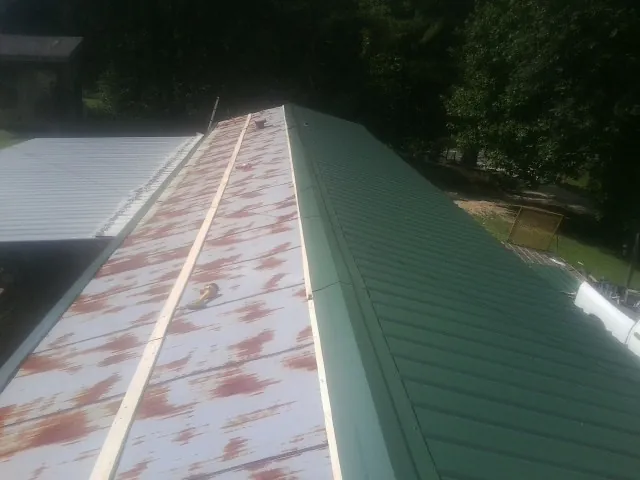Old rusted panels beside newly installed green metal roofing — Wind Damage Roof Repair by Roofing Brothers in Burlingham