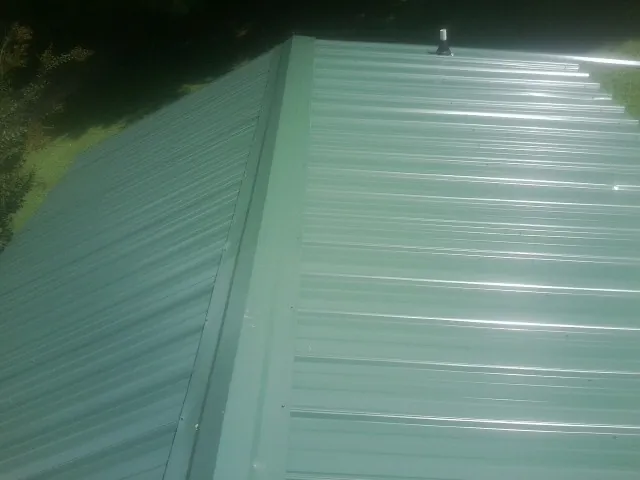 New green metal panels meeting at the ridge of a roof — Flat Roof Repair work by our crew in Burlingham