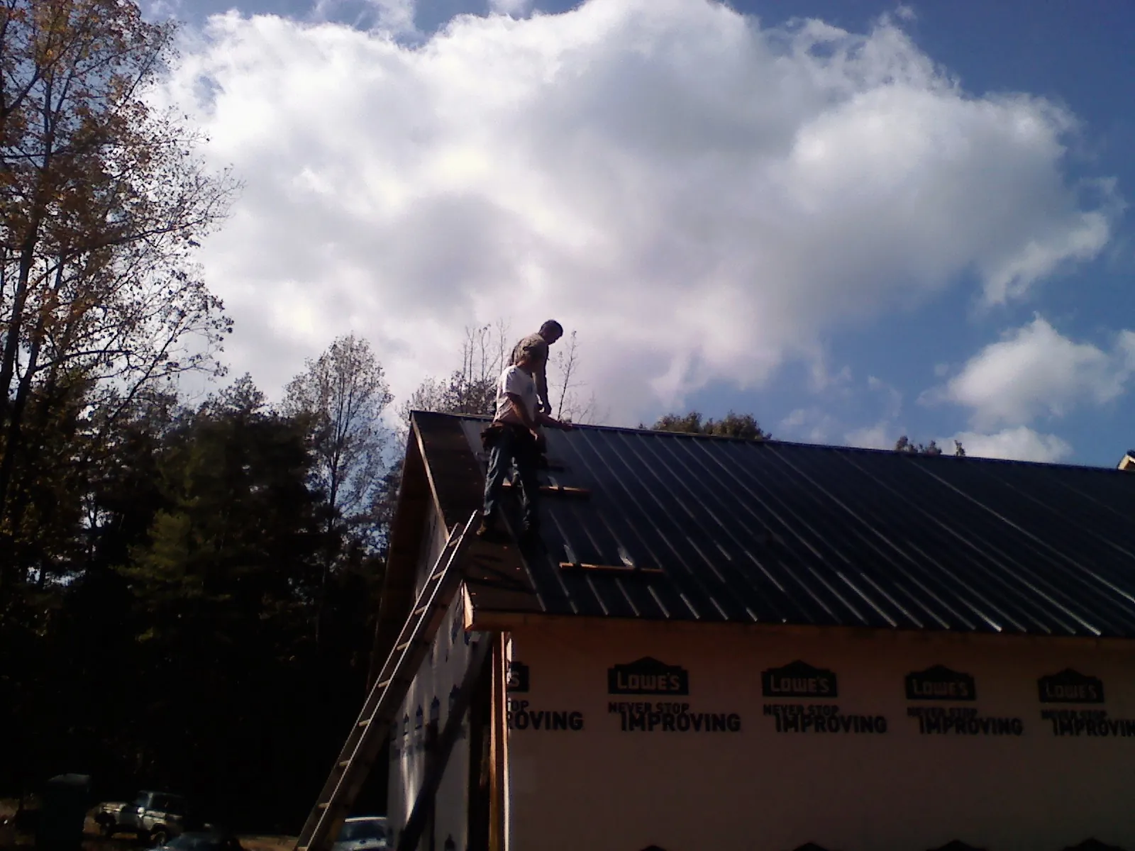 Roofer fastening dark metal panels high against a cloudy sky, from a Roof Inspection job in Burlingham