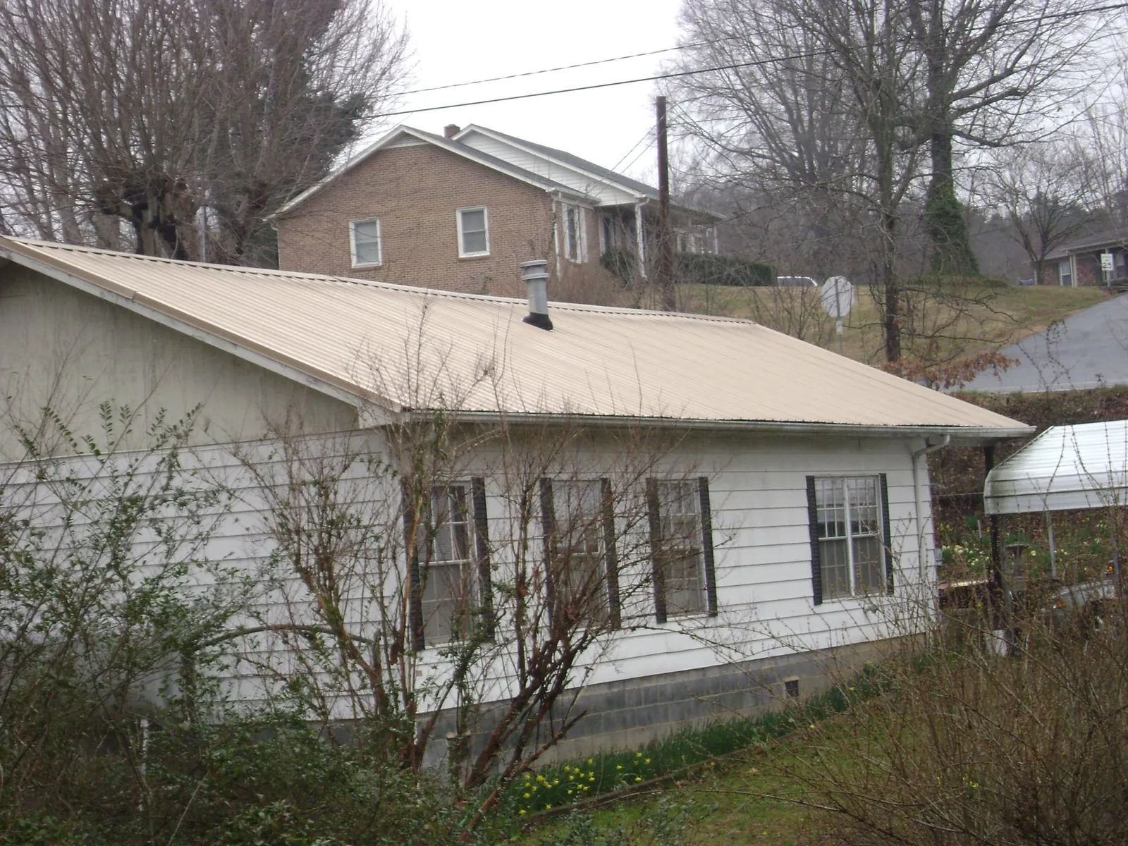 Tan metal roof on a white sided house set into a hillside — Commercial Roofing by Roofing Brothers in Burlingham