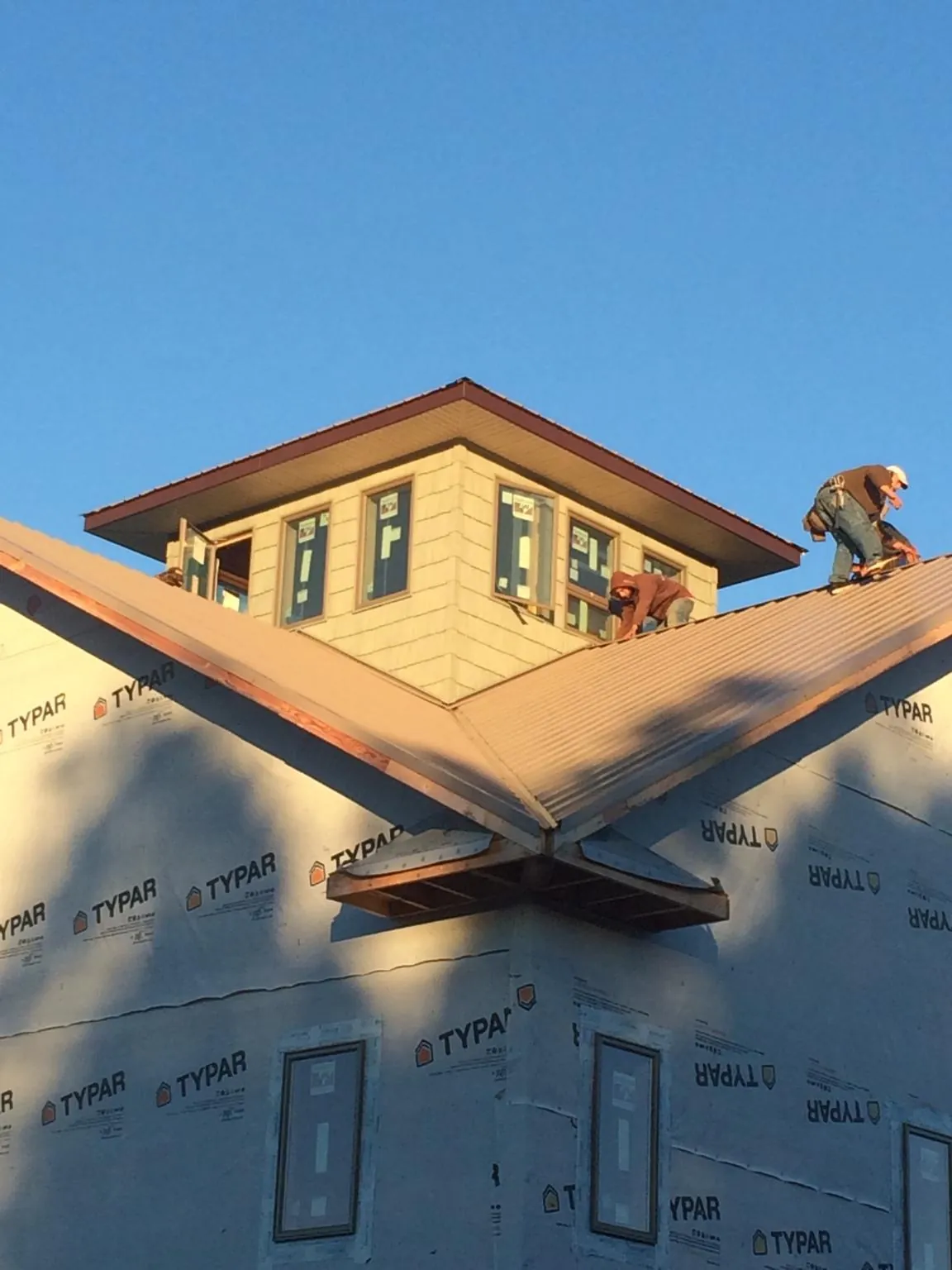 Roofers working around a rooftop cupola on a new metal roof at sunset — Roof Waterproofing in Burlingham by Roofing Brothers